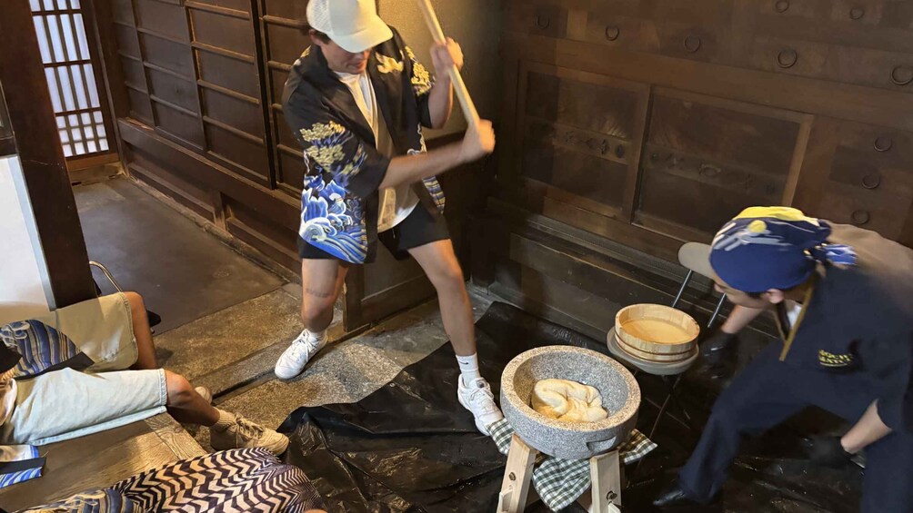 A person mashing food in a stone mortar, another person standing nearby, and a third person lying on the ground. 4