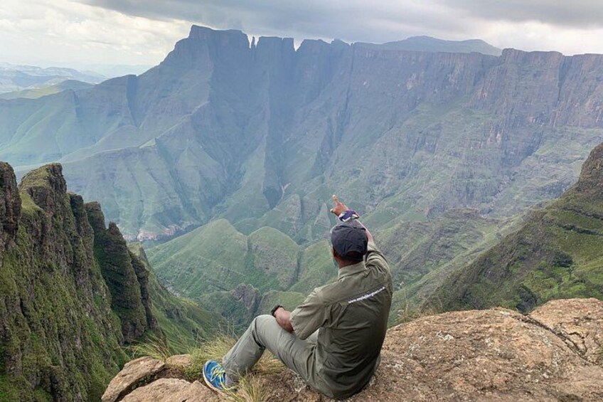 Eine Person sitzt auf einem Felsen und blickt auf eine gebirgige Landschaft. 1