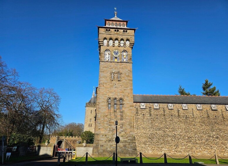 A historic stone tower with a clock, surrounded by a low stone wall and a chain barrier. 3