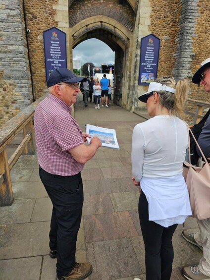 A man and a woman standing in front of a stone archway with bilingual welcome signs. 2