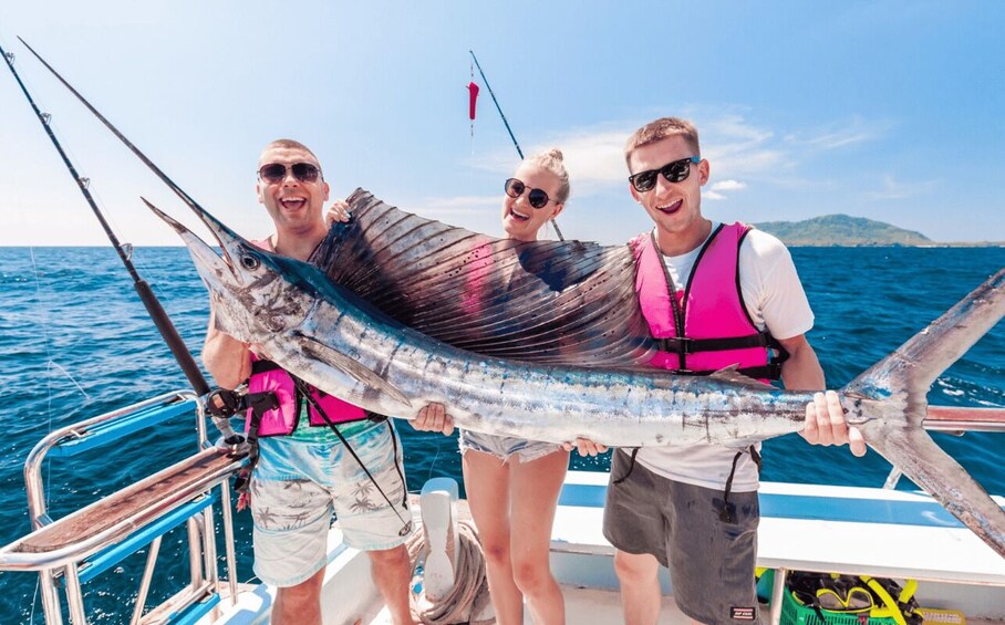 Three people on a boat holding a large fish. 1
