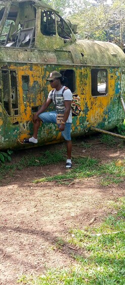 A person standing next to a rusted, abandoned aircraft with visible damage and peeling paint. 2