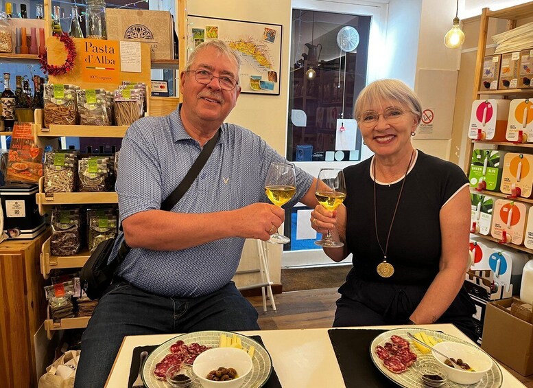 Two people sitting at a table with plates of food and glasses of wine in a store with shelves of products. 3