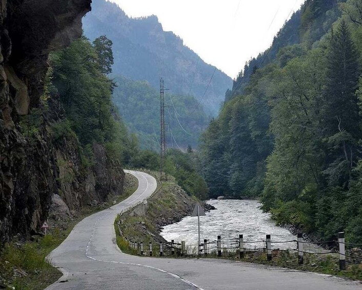 A winding road through a mountainous area with a river running alongside. 4