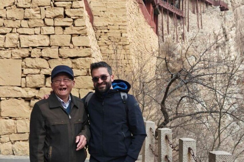 Two people standing in front of a stone wall with a metal structure above it. 3