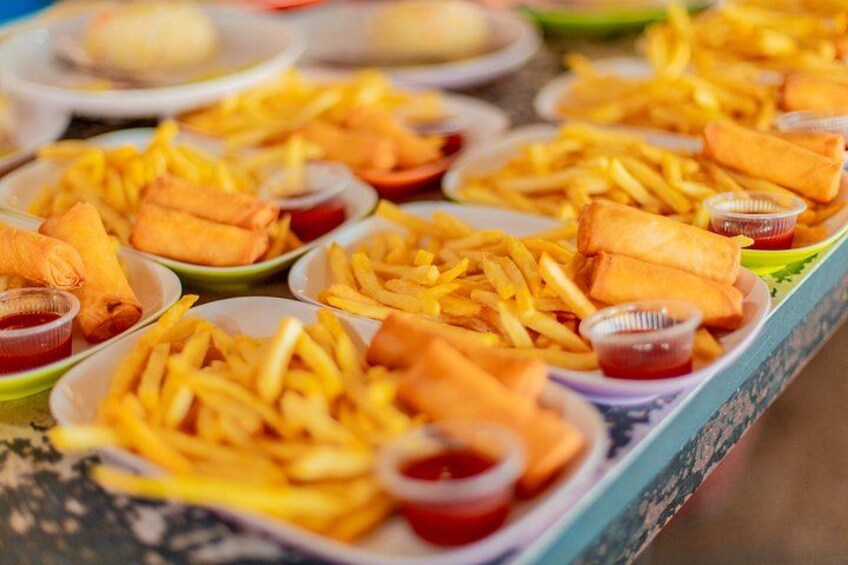 A table with plates of fried spring rolls, French fries, and small containers of sauce. 2