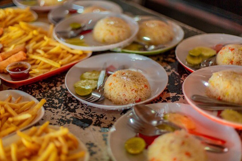 A table with plates of food, including rice balls, fries, and pickles. 3