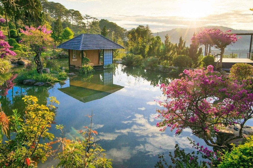 A traditional Japanese-style house by a reflective pond surrounded by lush greenery and flowering trees. 1
