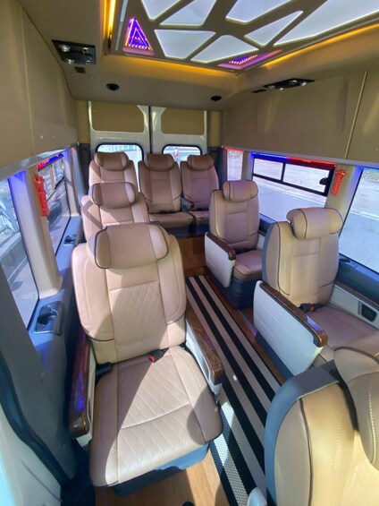 A bus interior with beige leather seats, a central aisle, and overhead lighting. 5