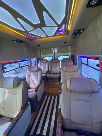 A bus interior with beige leather seats, a wooden floor, and a striped rug. 3