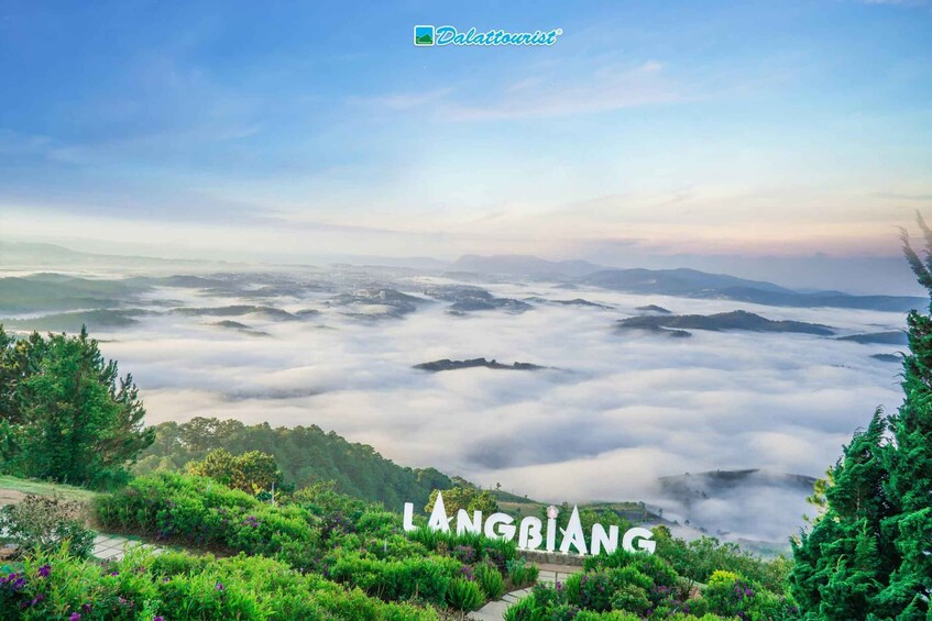 A landscape with a view of Langbiang, featuring lush greenery, a pathway, and a valley covered in clouds. 4