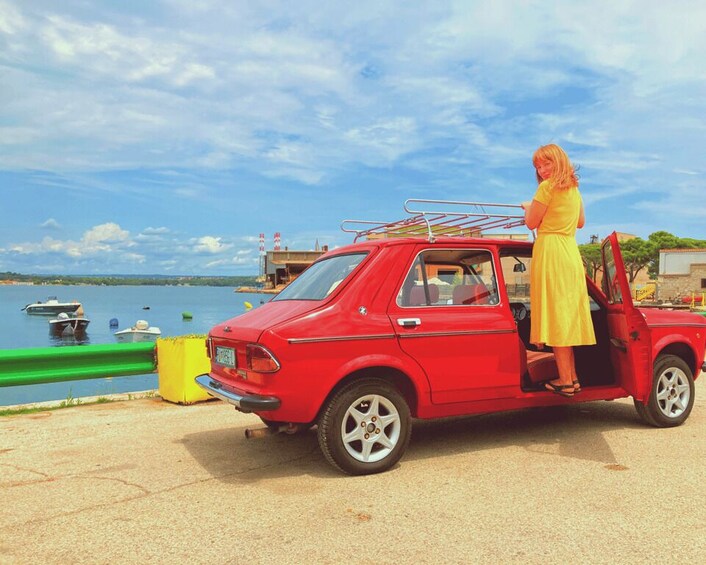 A red car parked by a body of water with a person standing next to it. 1