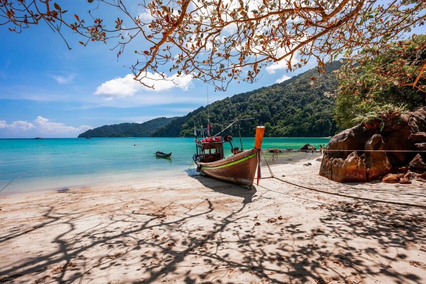 A beach with a boat, clear turquoise water, and a mountainous backdrop. 2
