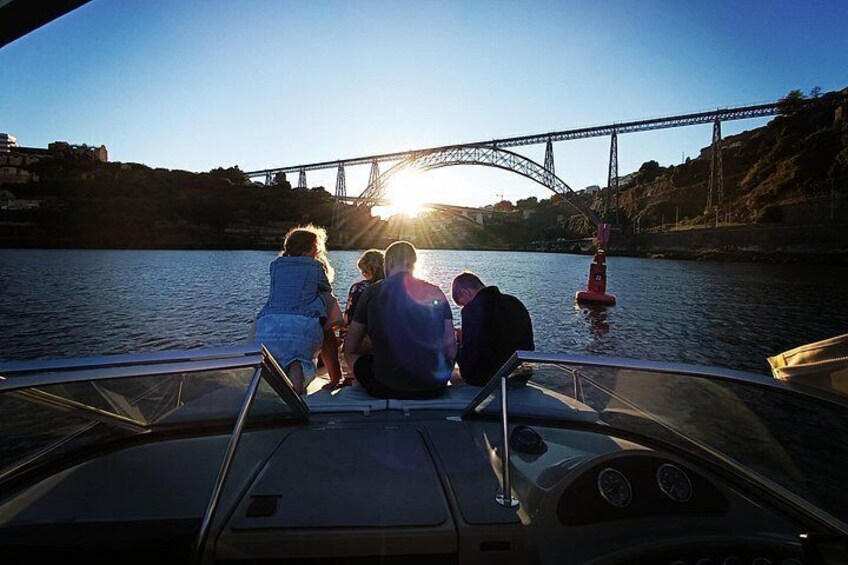 A boat with people on board, a bridge in the background, and the sun setting over the water. 4