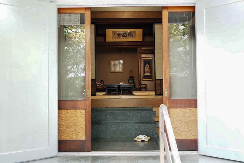 A traditional Japanese building entrance with a wooden sign, a small shrine, and a staircase leading inside. 4