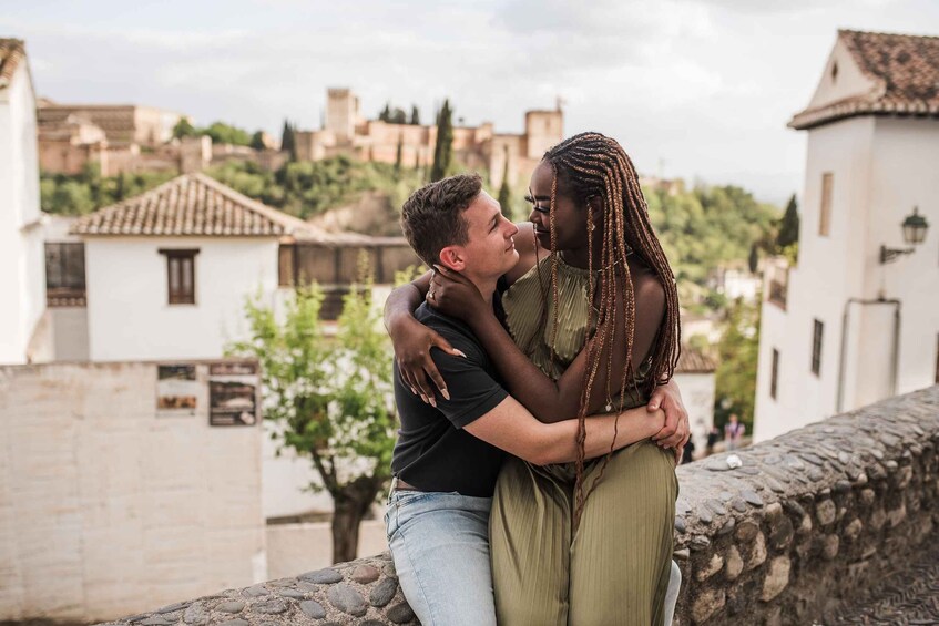 A couple embracing on a stone wall with a historic town in the background. 4
