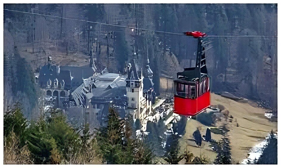 A red cable car ascending a mountain with a historic building in the background. 3