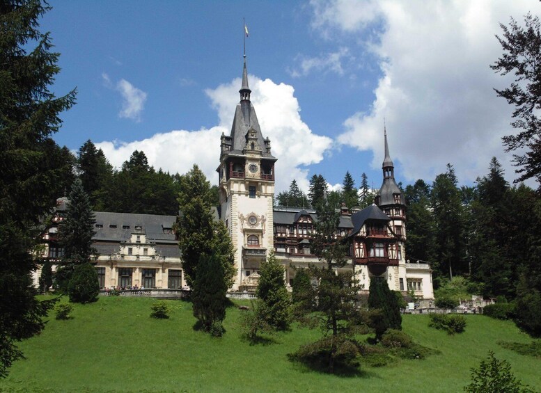A large, historic building with two prominent towers and a well-maintained garden. 1