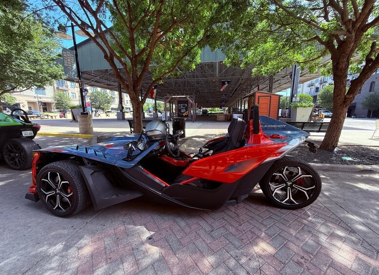 A red and black off-road vehicle parked on a paved area with trees and a building in the background. 5
