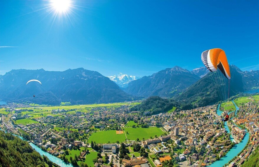 A mountainous landscape with a river, a town, and two paragliders. 1