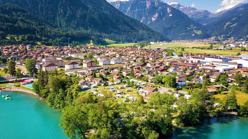 A lakeside town with residential buildings, a swimming area, and mountains in the background. 2