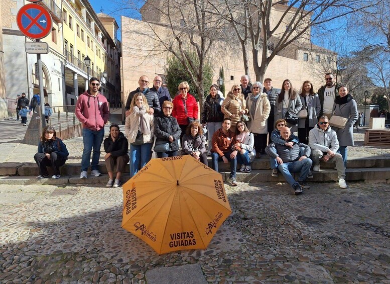 A group of people posing in front of a stone building with a no parking sign and an umbrella labeled "VISITAS GUIADAS". 2