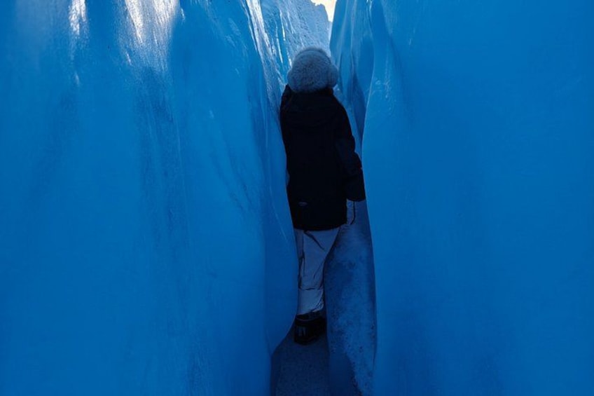 A person walking through a narrow, blue ice tunnel. 3
