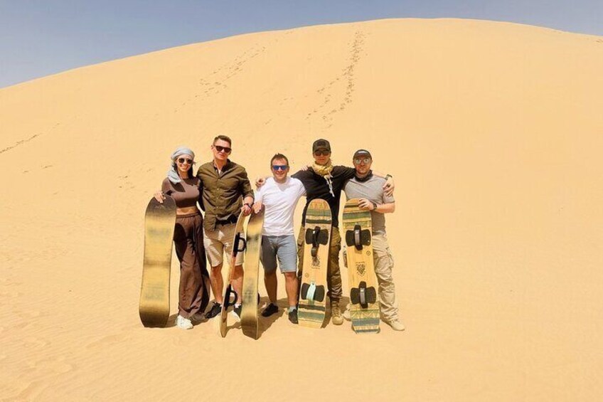 A group of people standing on a sand dune holding snowboards. 5