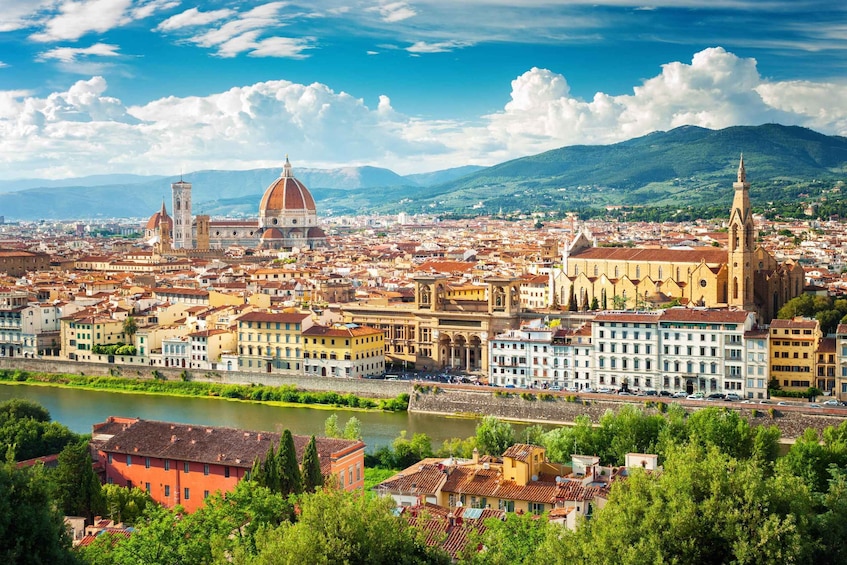 A panoramic view of a city with prominent historical architecture, including a cathedral with a large dome and a church with a tall bell tower, set against a backdrop of mountains and a river. 2