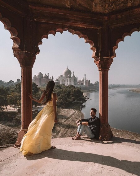 A person in a yellow dress standing and another person sitting under a pavilion with the Taj Mahal in the background. 4