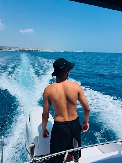 A person on a boat, wearing a hat, with a clear view of the sea and distant shoreline. 2