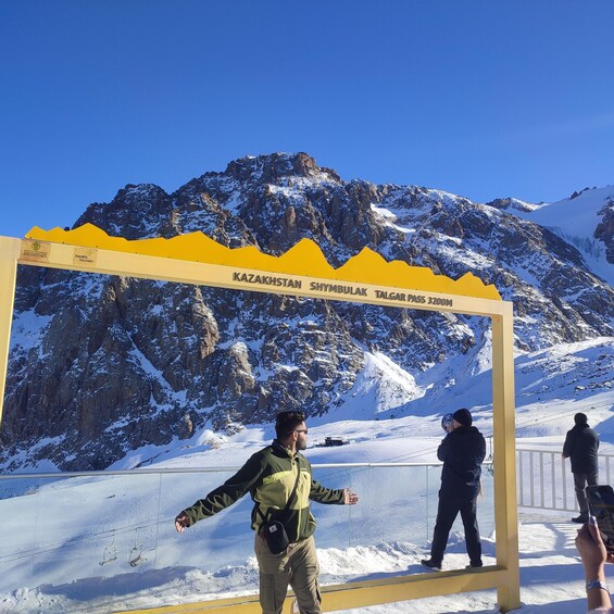 A snowy mountain landscape with a sign reading "KAZAKHSTAN SHYMBULAK TALGAR PASS 3200M". 3