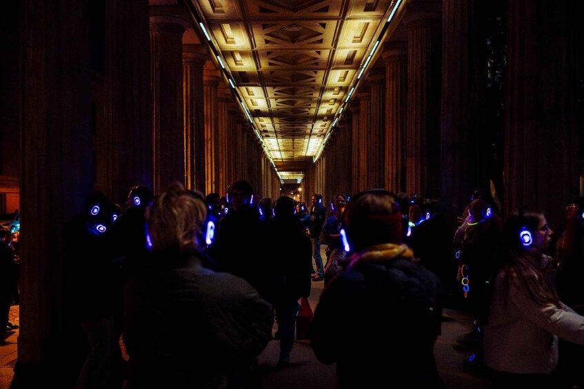 A group of people in a dimly lit corridor with a high ceiling and wooden columns. 2