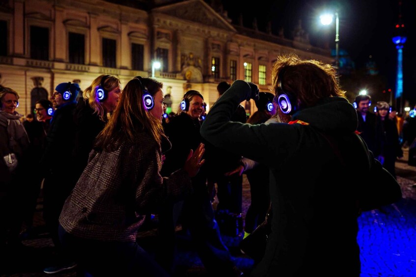 A group of people wearing headphones with blue lights, standing in front of a historic building at night. 4