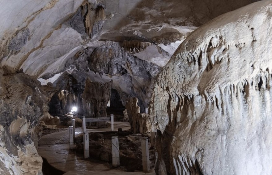 A cave with stalactites and stalagmites, a wooden platform, and a flashlight illuminating the area. 4