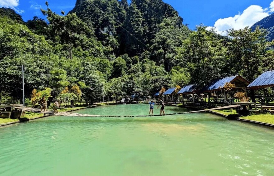 A calm lake with people playing, surrounded by lush greenery and a mountain in the background. 1