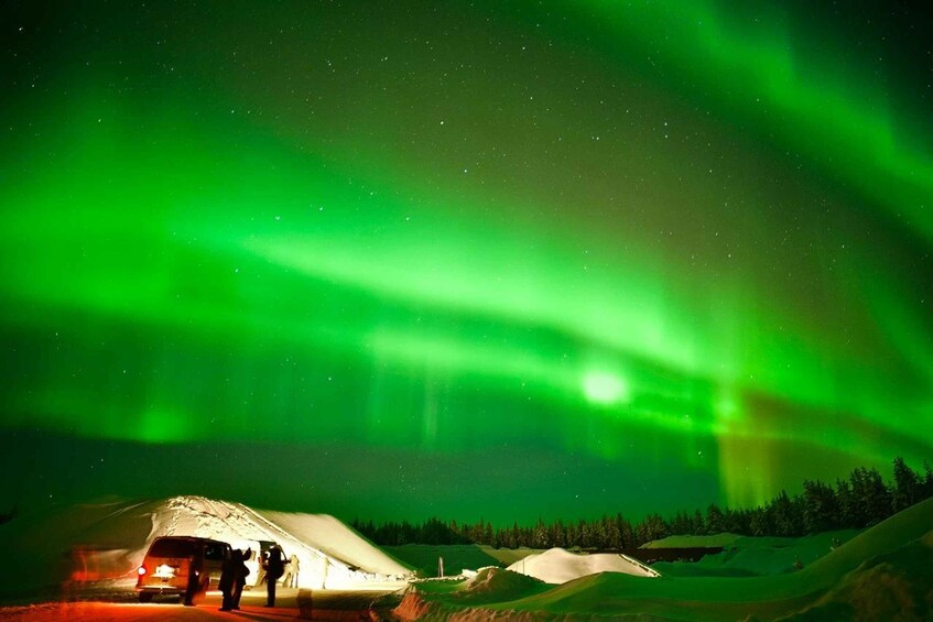 A snow-covered landscape with a tent and a vehicle under a green aurora display. 5
