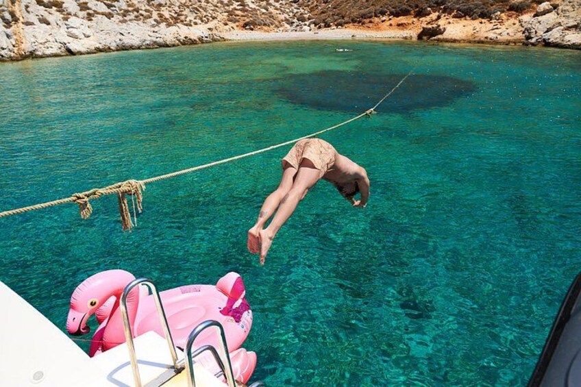 Una persona haciendo bungee jumping desde un barco hacia agua turquesa cristalina, con un flotador de flamenco rosa. 5
