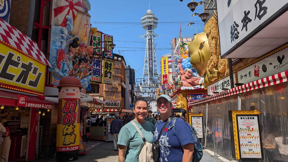 A bustling street with colorful signs and a prominent tower in the background. 5