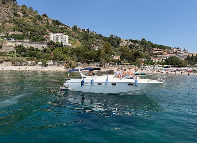 A boat with people on it near a beach with buildings in the background. 1
