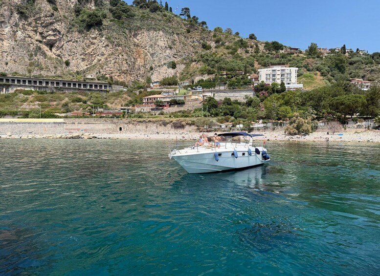 A boat on calm water with a rocky hillside and buildings in the background. 2