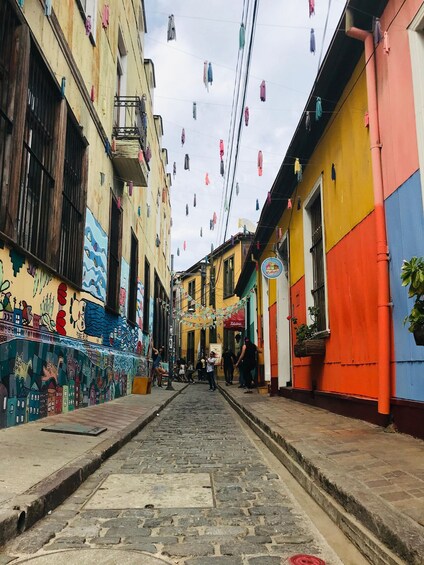 A narrow cobblestone street lined with colorful buildings, some with murals and hanging laundry. 3