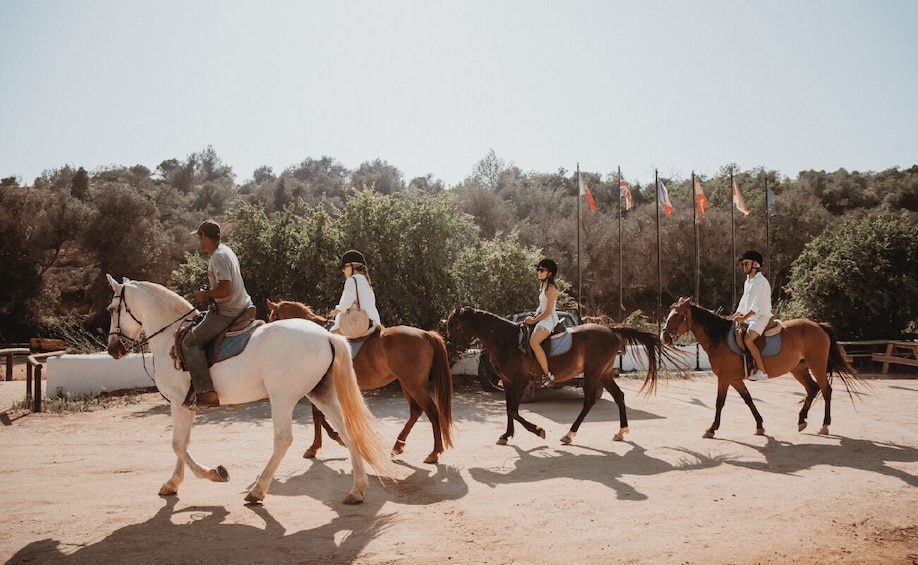 A group of people riding horses in an outdoor arena with flags in the background. 2