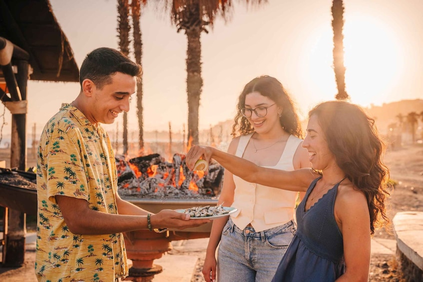 A person serving food to two others at a barbecue with a fire in the background. 2