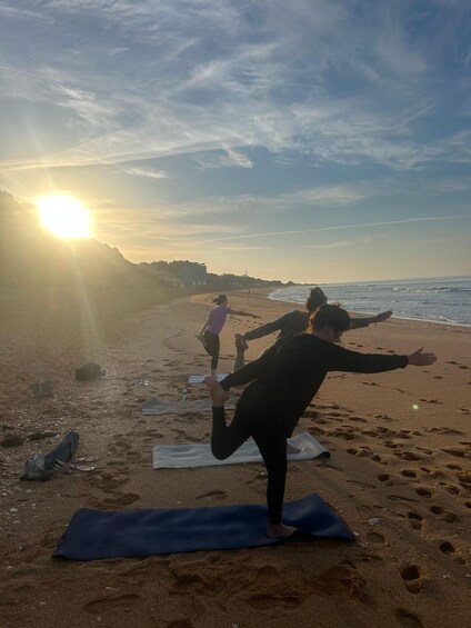 People practicing yoga on a beach with the sun setting in the background. 1