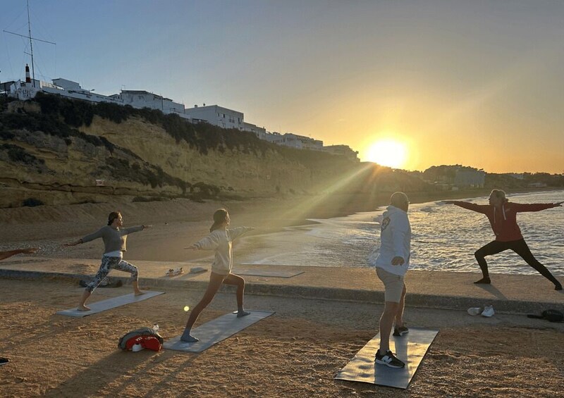 A group of people practicing yoga on mats by the seaside during sunset. 2
