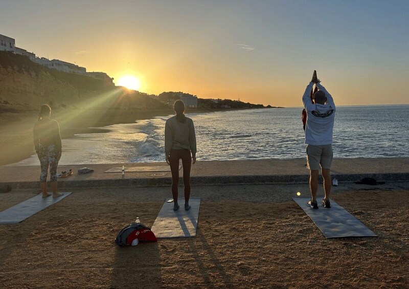 Three people on yoga mats at the beach during sunset. 3