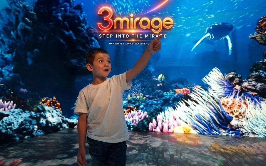 A child pointing at an aquarium exhibit with a sign reading '3mirage Step into the Mirage Immersive Light Experience.' 1