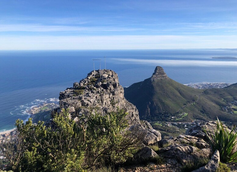 A rocky mountain peak with a cross on top, overlooking a coastal city and ocean. 4