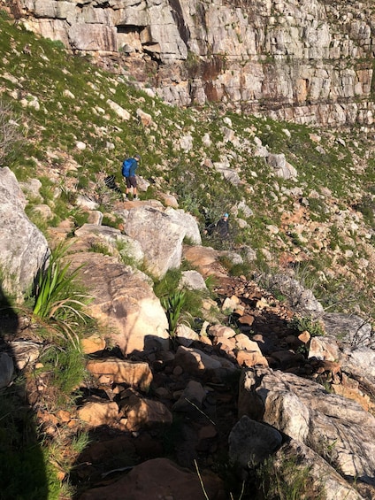 Hikers on a rocky trail with large boulders and sparse vegetation. 2
